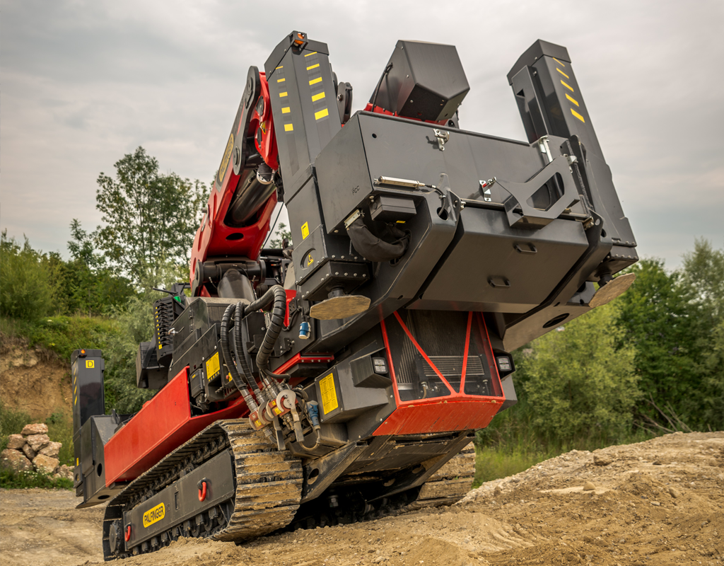 PALFINGER PCC115 crawler crane travelling over uneven terrain with outriggers folded for transport.