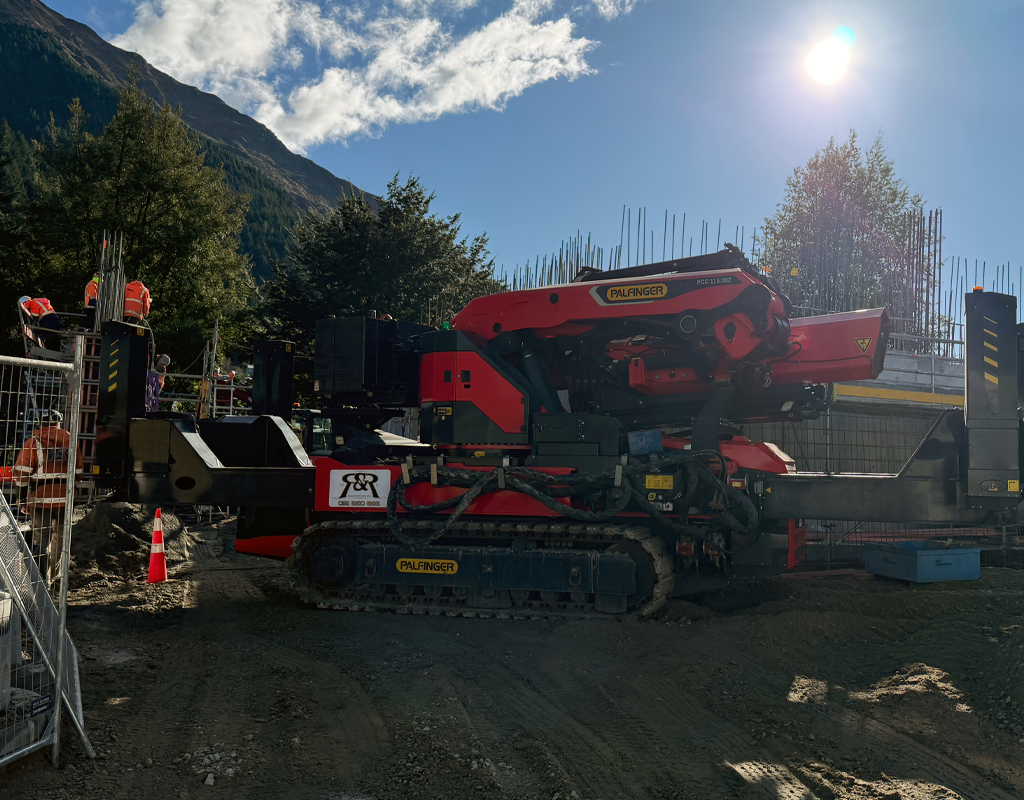 PALFINGER PCC115 crawler crane set up on a construction site in mountainous terrain under a clear blue sky.